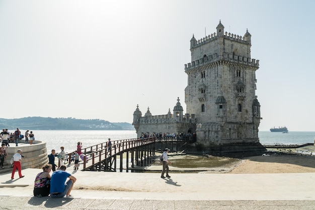 People walk by Torre de Belem famous landmark of Lisbon Portugal