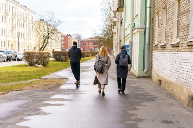 People walk down street on sidewalk with backpacks on their backs on sunny spring day a man rides a ...