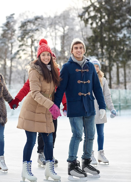 people, winter, friendship, sport and leisure concept - happy friends ice skating on rink outdoors