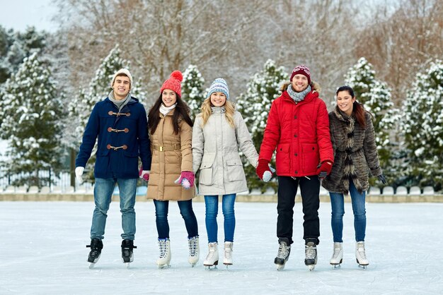 people, winter, friendship, sport and leisure concept - happy friends ice skating on rink outdoors