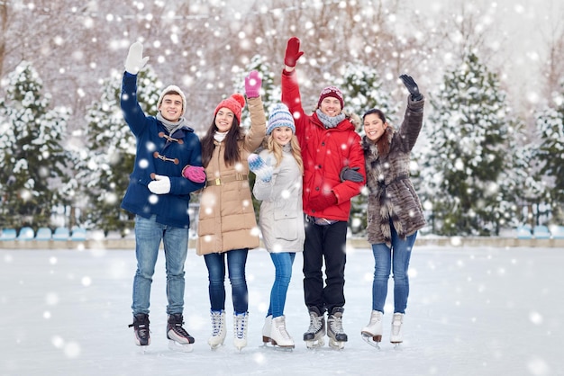 people, winter, friendship, sport and leisure concept - happy friends ice skating and waving hands on rink outdoors