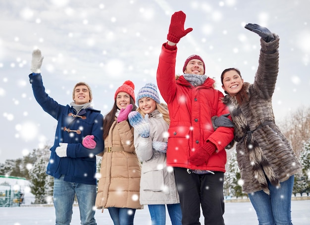 people, winter, friendship, sport and leisure concept - happy friends waving hands on ice rink outdoors