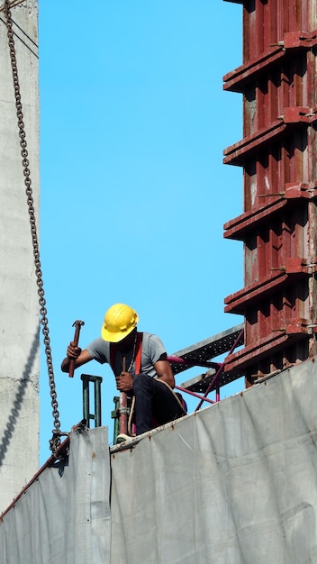 People working on construction site with yellow helmet and safty rope equipment and covering the building with grey color vinyl and blue sky.