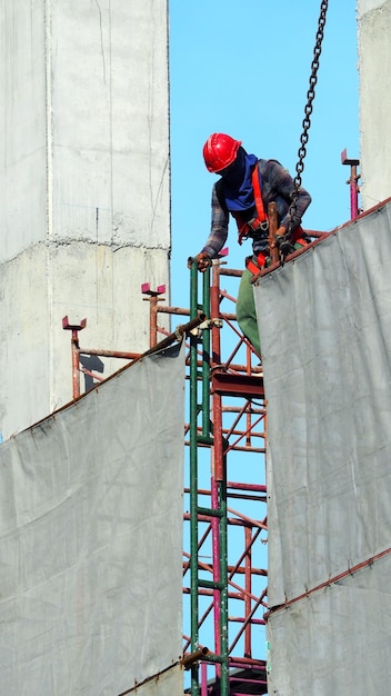 People working on construction site with yellow helmet and safty rope equipment and covering the building with grey color vinyl and blue sky.