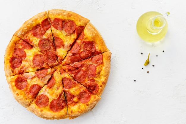 Peperoni pizza with olive oil and pepper on a light table.