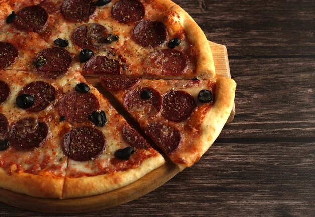 Pepperoni pizza with sausage and olives on a dark wooden background