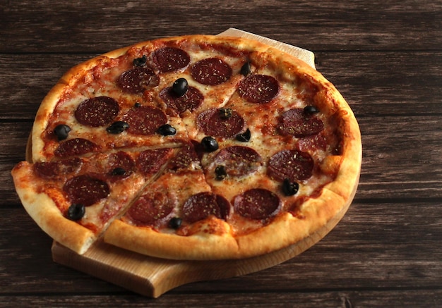 Pepperoni pizza with sausage and olives on a dark wooden background