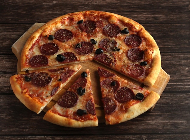 Pepperoni pizza with sausage and olives on a dark wooden background