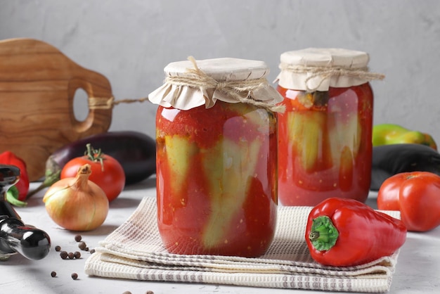 Peppers stuffed with eggplant and onions in tomato sauce in two glass jars on gray background