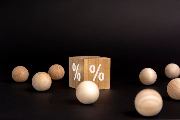 Percent sign on wooden cube on black background with wooden balls concept of sale and discount