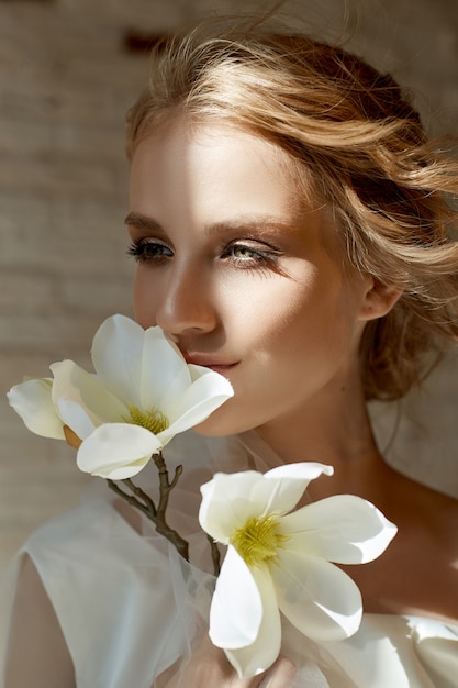 Perfect bride with jewels, a portrait of a woman in a long white dress. Beautiful hair and clean delicate skin. Wedding hairstyle blonde woman. woman with a white flower in her hands