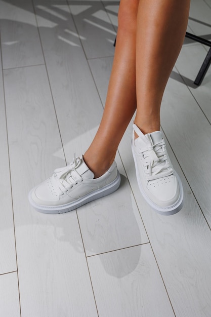 Perfect female legs in white classic sneakers Beautiful female legs in summer shoes in white shoes