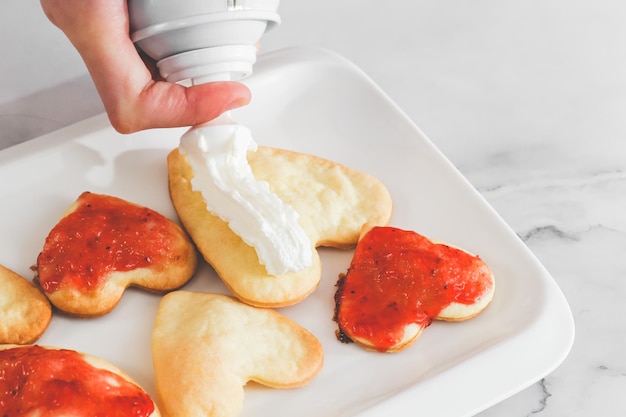 Not perfect freshly baked heart cookies in a white plate with strawberry jam