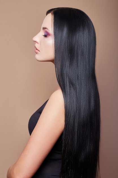 Perfect straight long hair woman, lamination and straightening hair. Strong black hair roots. Profile of brunette woman on a beige background