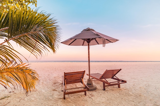 Perfect tropical sunset scenery, two sun beds, loungers, umbrella under palm tree. White sand, sea