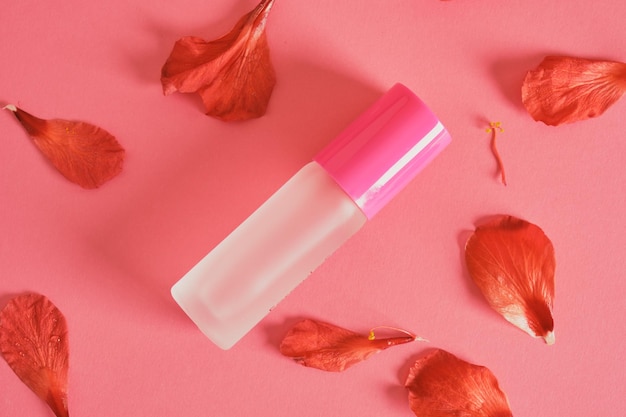 Perfume bottle and hibiscus flower petals on pink background