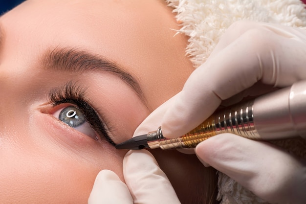 Permanent eye makeup close up shot on cosmetologist applying tattooing of eyes