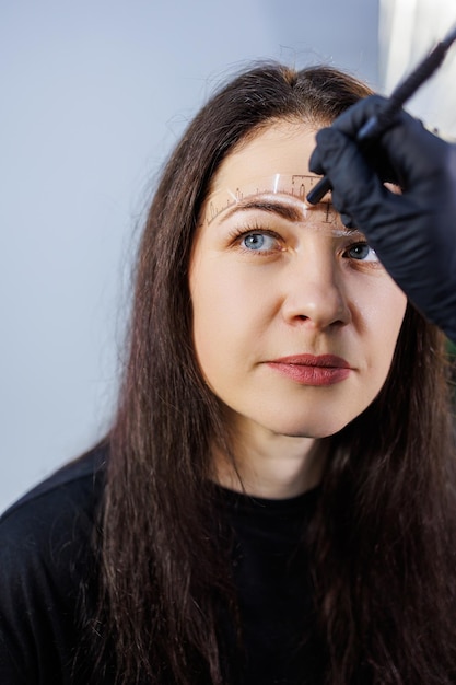 A permanent makeup artist marks a woman's eyebrows with a pencil Cometological procedure of permanent makeup Care for a woman's face