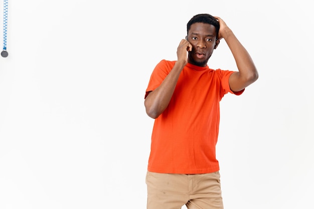 Perplexed man of African appearance talking on the phone on a light background and Tshirt shorts