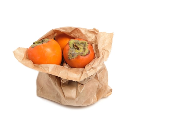 Persimmon fruit in a grocery paper bag on a white background.