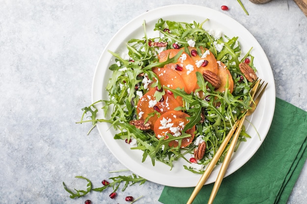 Persimmon salad with arugula, nuts, goat cheese, pomegranate. Healthy vegetarian food salad concept.