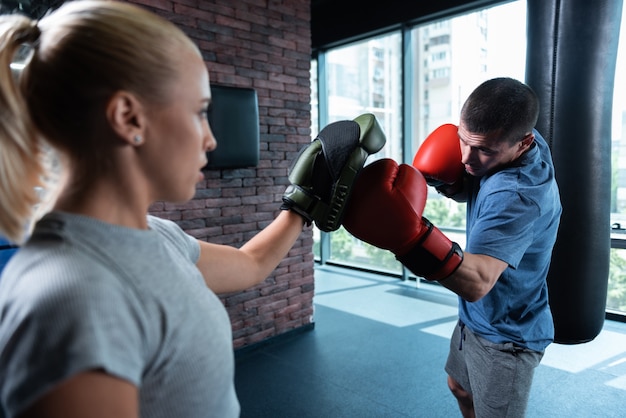 Photo persistent man. persistent athletic man boxing hard in gym with city view along with his female trainer