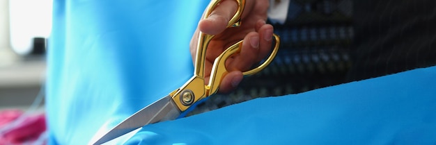 Person cutting blue cotton cloth with scissors tool for further sewing