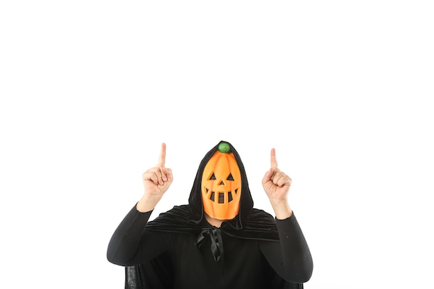 Photo person dressed in pumpkin jack-o.-lantern mask and hooded velvet cape, pointing fingers up with copy space, on white background. carnival, halloween and day of the dead concept.