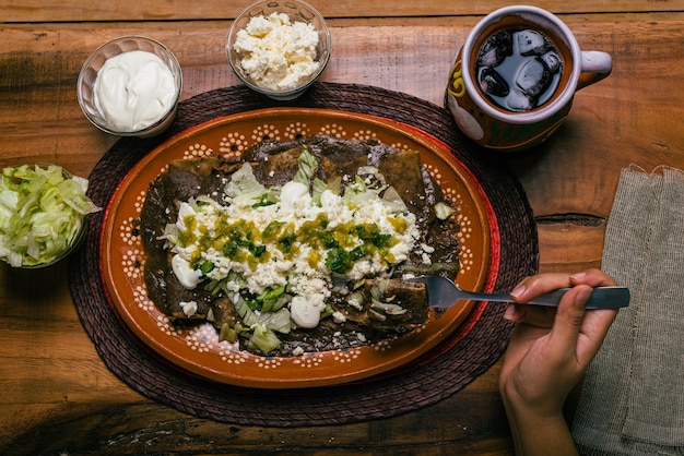 Person eating Enfrijoladas served in a clay dish Mexican food Bean tacos with cream and cheese