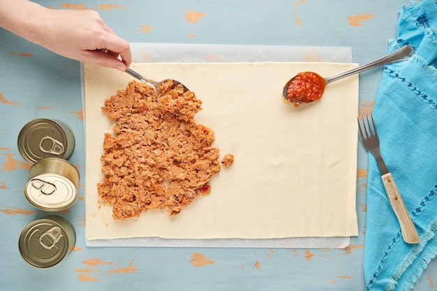 Person fills a dough with tuna and tomato to prepare a Galician empanada