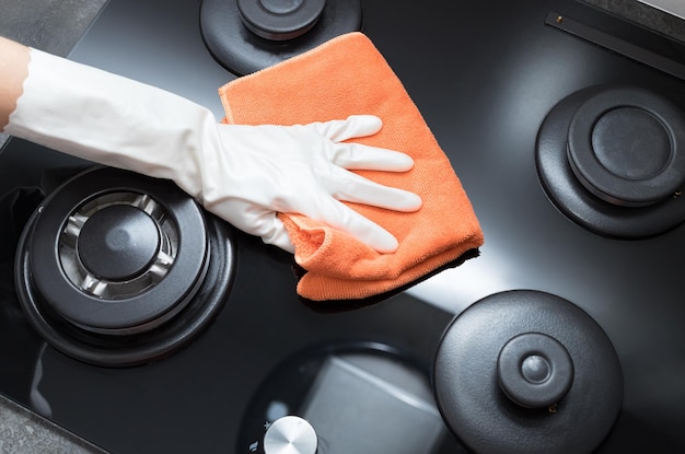 Person hand in rubber glove holding rag and wiping gas stove top House cleaning concept