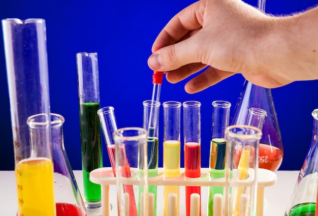 Person hand working in chemistry lab over blue background. Glassware and biology equipment