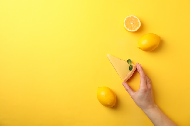 Person hold slice of lemon tart on yellow, top view