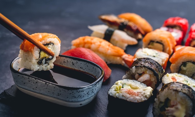 Person hold sushi maki roll with chopstick and put it to soy sauce oriental japanese healthy cuisine