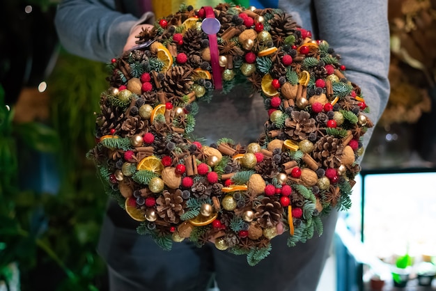 Person holding beautiful and colourful hand made Christmas wreath, green spruce branches decorated with pine cones and other decorations. Christmas chaplet in hands.