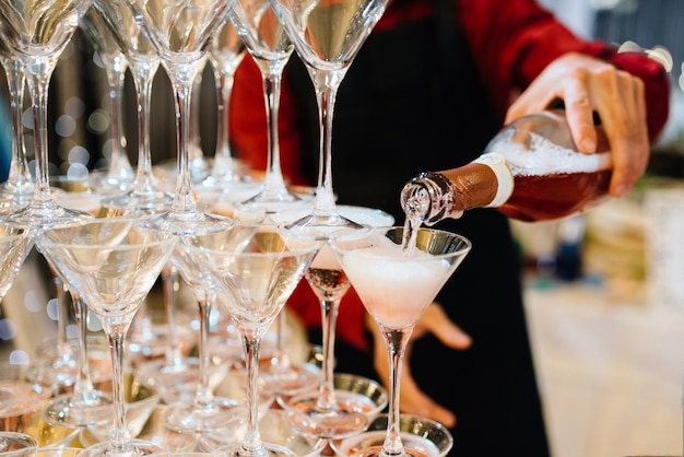 Person holding bottle of champagne and serving pyramid of delicious drink