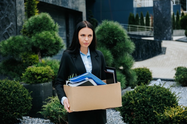 A person holding a box outside their former workplace after being fired and feeling jobless Starting Over Woman Outside with Box of Possessions After Job Loss