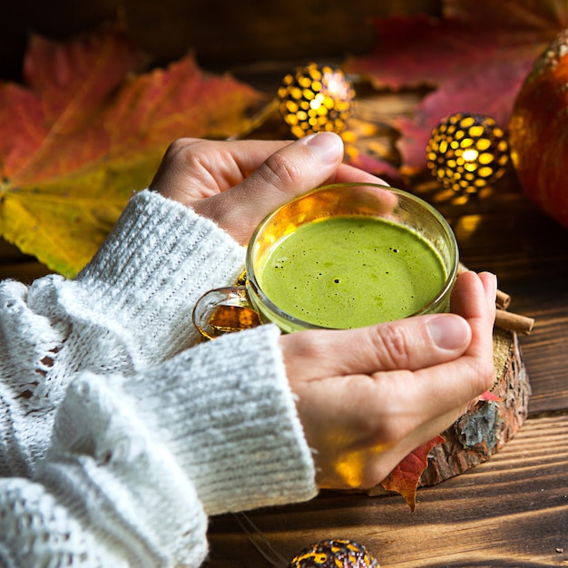 Person holding cup of matcha tea with autumn decor