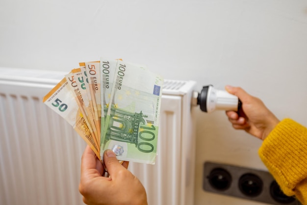 Person holding euro banknotes near heater at home