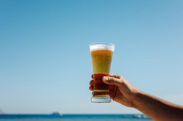 The person holding a glass of beer against the background of the sea