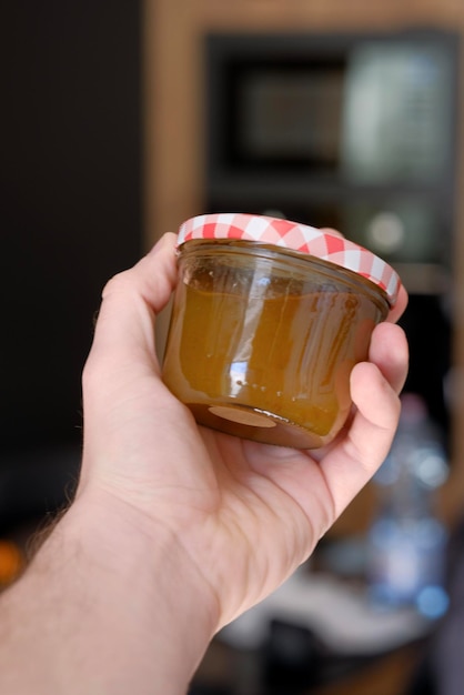 A person holding a jar of honey with a red and white lid.