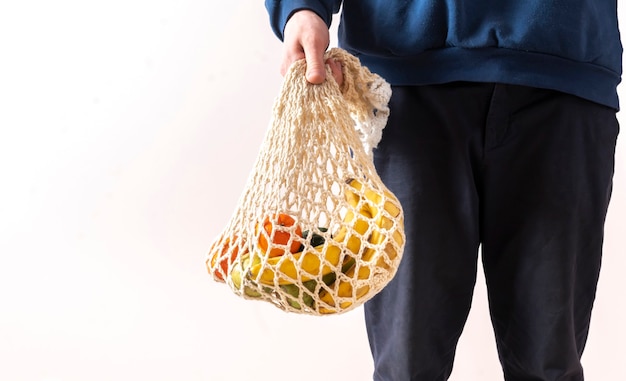 A person holding a mesh bag with fresh raw food fruits and vegetables, eco friendly zero waste conversation