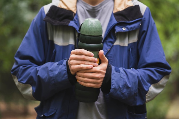 A person holding a metal thermos with hot water outdoors