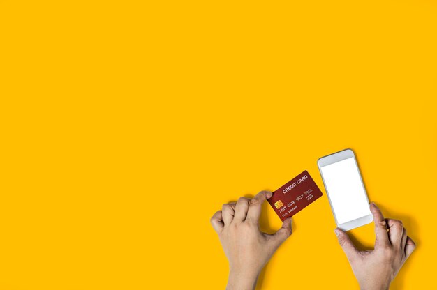 Person holding a red credit card and a mobile phone, images for online shopping advertisements, pay with credit card, Isolated on yellow background and clipping path.