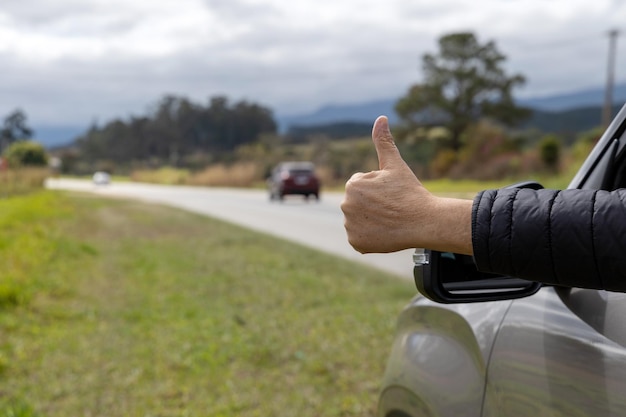 Person indicating positive from inside the car Thumbs up sign with hand on the road traveling.