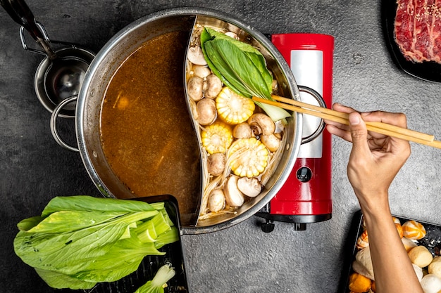 Photo a person is cooking a dish with a red pot and a green leaf