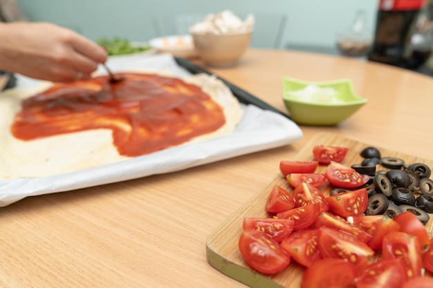 A person is making a pizza with tomatoes on a cutting board.