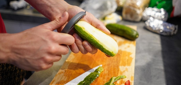 Person is peeling a cucumber Person peels a cucumber over the wooden cutting board Peeling vegetab