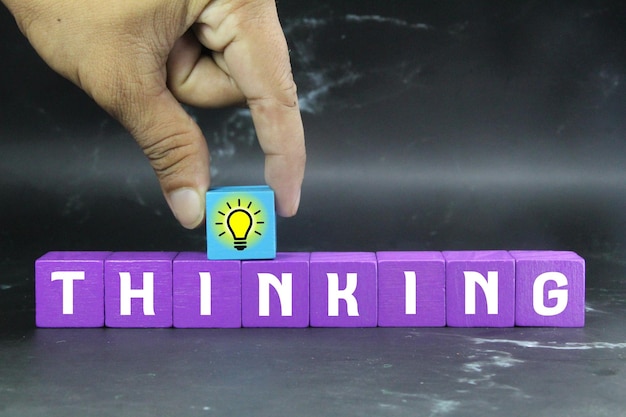 A person is putting a lightbulb on a purple cube that says thinkin.