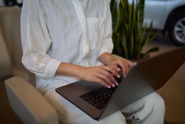 A person is seen typing on a laptop in a modern office setting with cars in the background